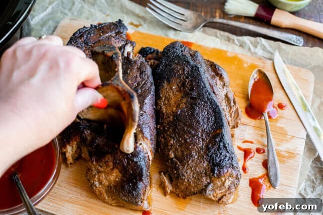 Melt In Your Mouth Pulled Pork Slow Cooker Or Oven 13 pulling the bone out of cooked pork shoulder on a cutting board.
