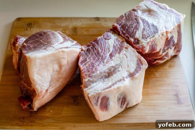 Melt In Your Mouth Pulled Pork Slow Cooker Or Oven 14 raw pork shoulder on a cutting board, in 3 pieces.