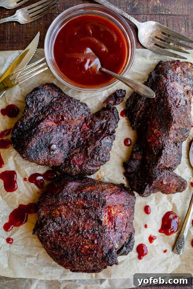 Melt In Your Mouth Pulled Pork Slow Cooker Or Oven 17 oven roasted pork shoulder in 3 pieces on parchment paper with bowl of bbq sauce.