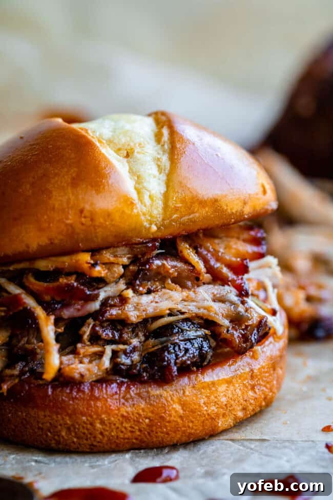 Melt In Your Mouth Pulled Pork Slow Cooker Or Oven 3 oven pulled pork on a hamburger bun on parchment paper.