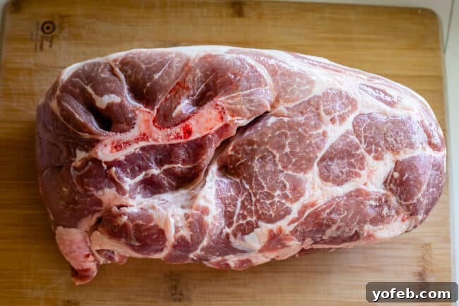 Melt In Your Mouth Pulled Pork Slow Cooker Or Oven 7 raw pork shoulder on a wooden cutting board, bone in.