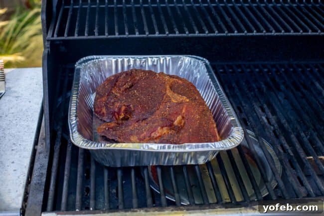 Smoky Perfection: The Ultimate Pulled Pork 20 partially cooked pork shoulder in a 9x13 inch disposable pan on a grill.