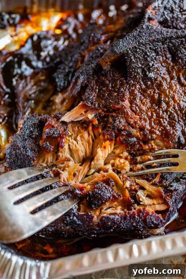 Smoky Perfection: The Ultimate Pulled Pork 23 two forks shredding smoked pulled pork with blackened bark edge in an aluminum pan.