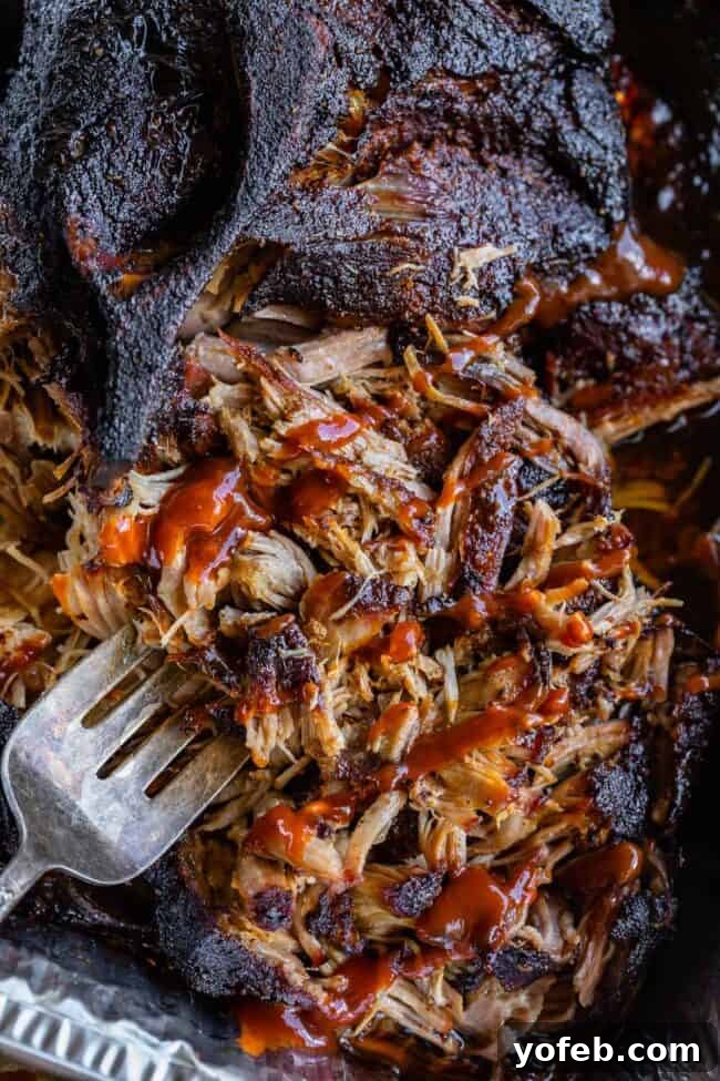 Smoky Perfection: The Ultimate Pulled Pork 25 fork sticking into shredded smoked bbq pulled pork topped with bbq sauce.