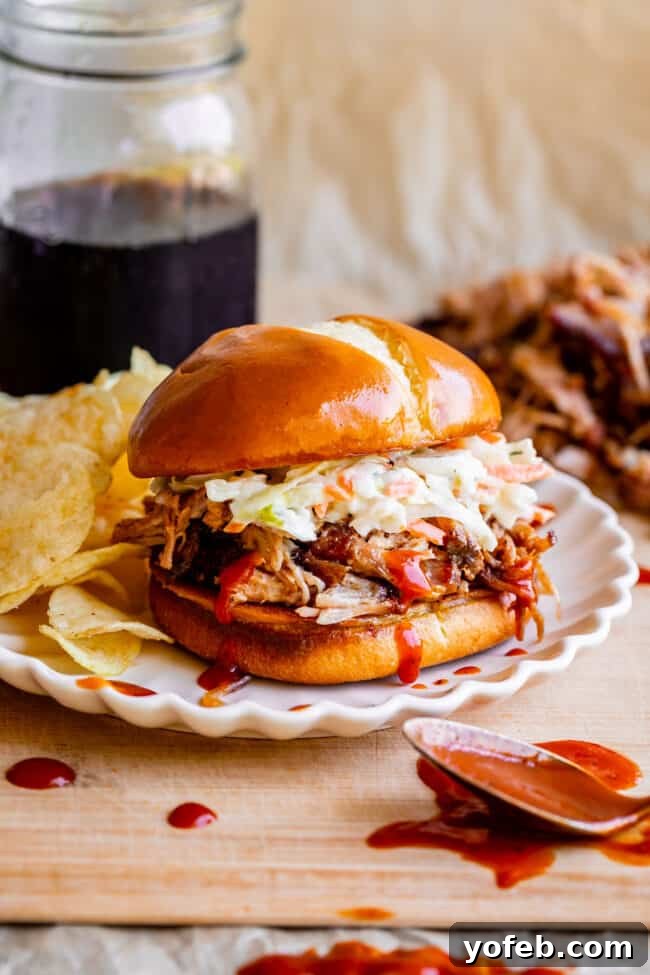 Smoky Perfection: The Ultimate Pulled Pork 27 smoked pulled pork sandwich with coleslaw on a white plate with soda and chips.