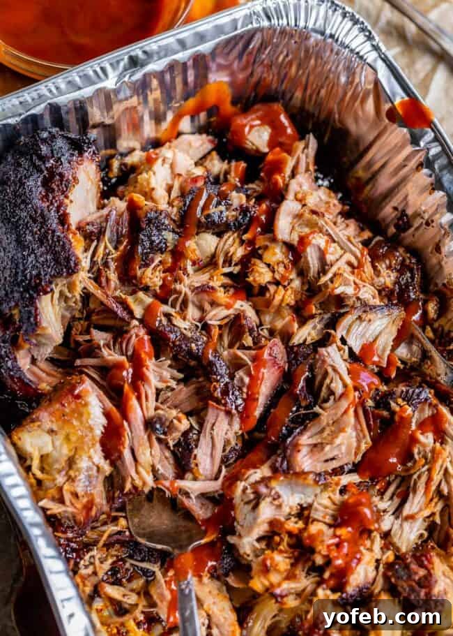 Smoky Perfection: The Ultimate Pulled Pork 6 Shredded smoked pulled pork drizzled with bbq sauce in an aluminum pan.