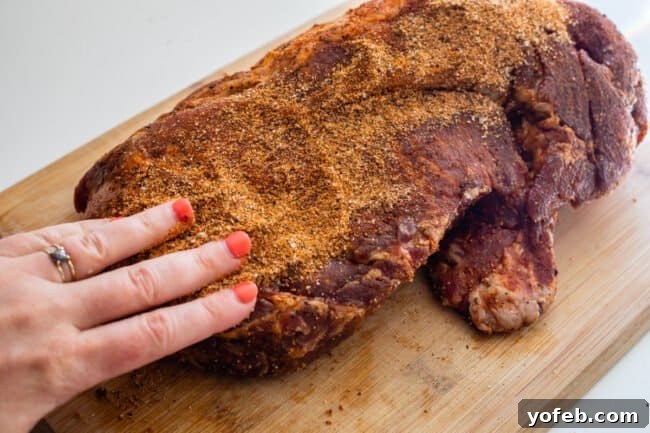Smoky Perfection: The Ultimate Pulled Pork 10 using fingers to rub spice rub into pork shoulder on cutting board.