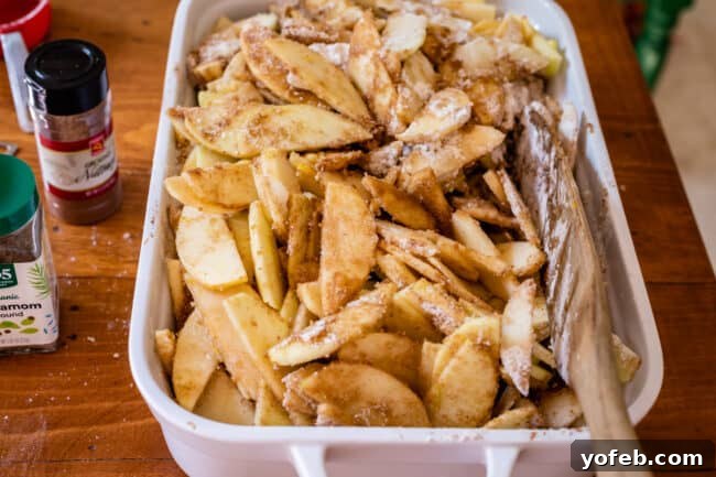 Effortless Homemade Apple Cobbler 15 Raw apples coated in flour and sugar in a white casserole dish, ready for topping.