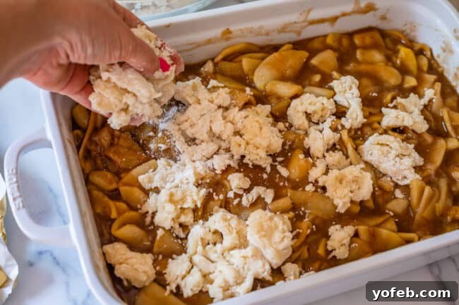 Effortless Homemade Apple Cobbler 19 Adding a floury, shaggy biscuit topping to an apple cobbler in a white casserole dish.