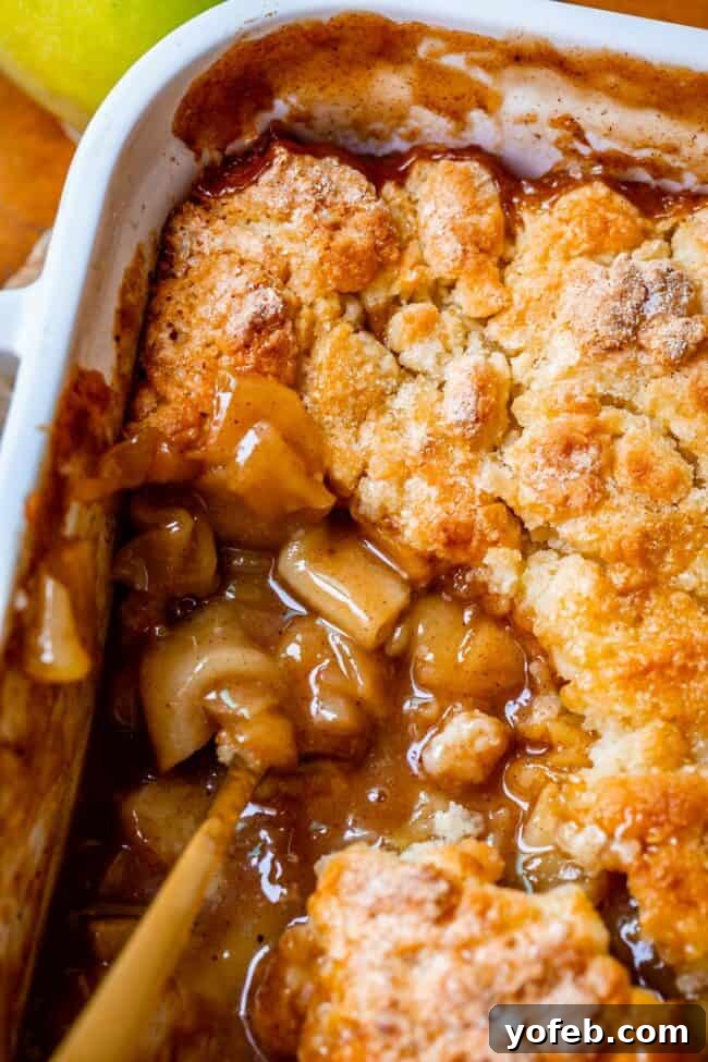 Effortless Homemade Apple Cobbler 3 The best homemade apple cobbler recipe in a white baking dish with a gold spoon scooping into the apples.