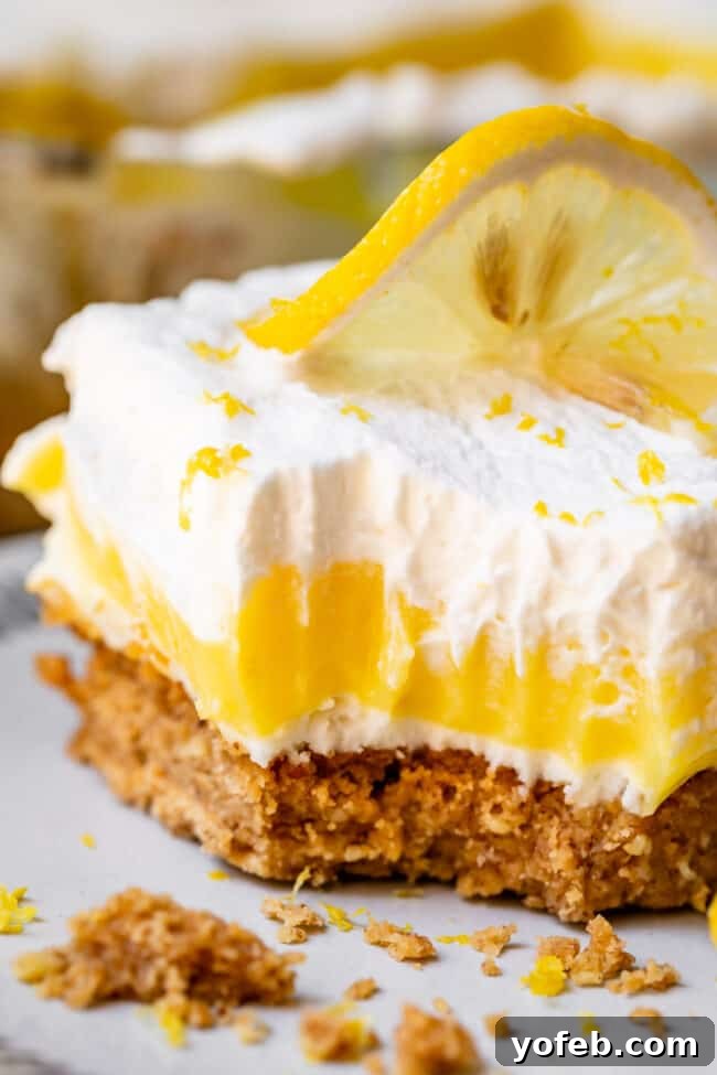 Sunshine Lemon Delight 2 A beautifully layered Lemon Lush Dessert slice showcasing the crumbly crust, creamy white layer, yellow pudding, and whipped cream topping.