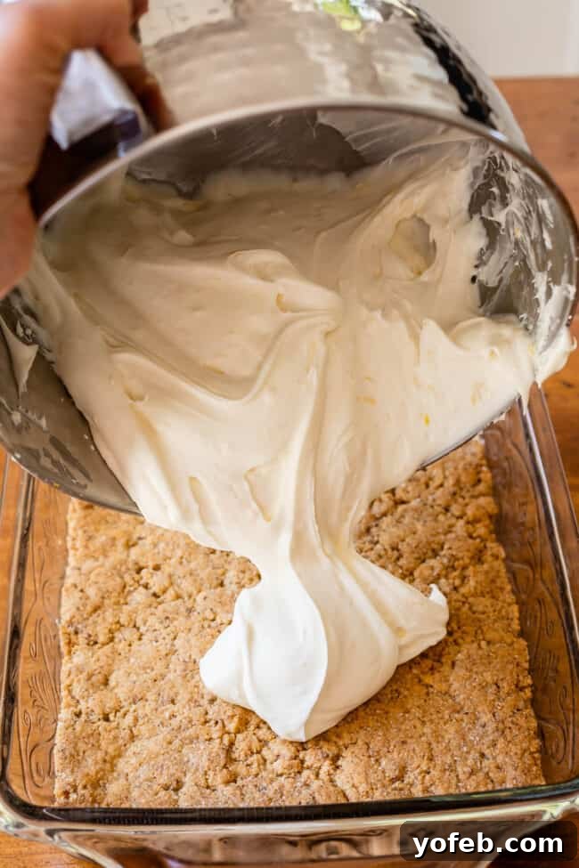 Sunshine Lemon Delight 12 Spreading cream cheese filling over the cookie crust in a 9x13-inch baking dish, creating the second layer.