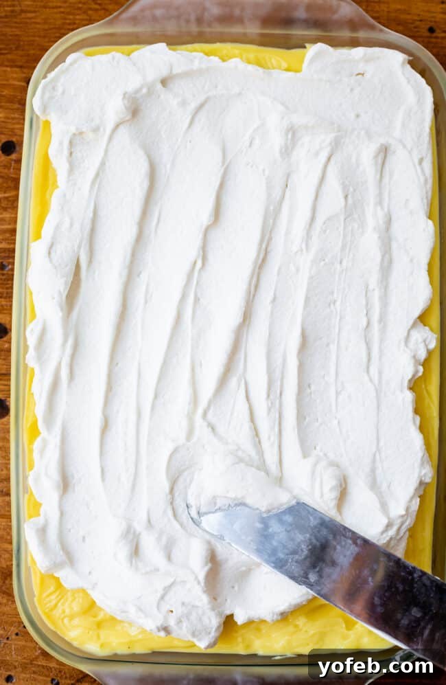 Sunshine Lemon Delight 15 Spreading fluffy whipped cream evenly over the chilled lemon pudding layer in a casserole dish.