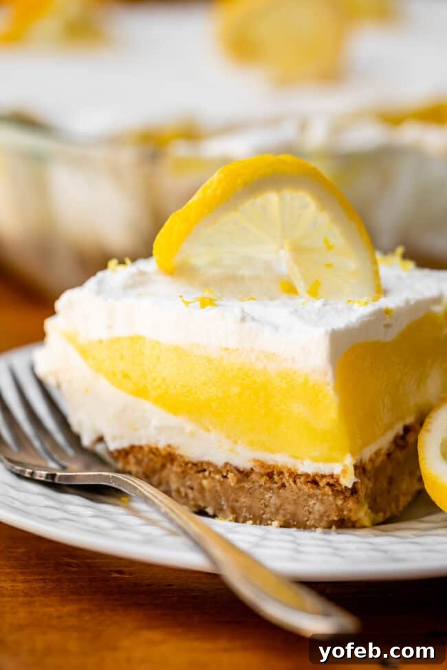 Sunshine Lemon Delight 5 A diagonal slice of Lemon Lush Dessert on a white plate with a silver fork, highlighting the crisp crust and creamy layers.