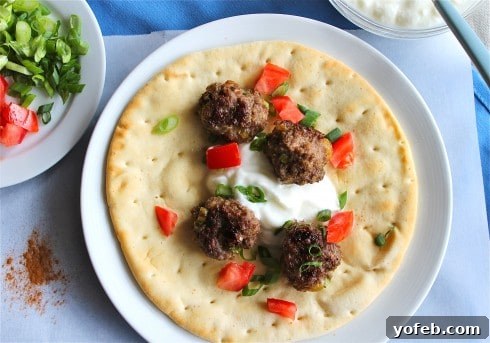 Spiced Lamb Kofta Gyros 3 Close-up of delectable Lamb Meatballs nestled in warm pita bread, surrounded by fresh gyro fixings on a pristine white paper, set against a charming blue tablecloth.