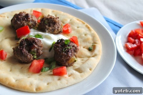Spiced Lamb Kofta Gyros 4 A vibrant plate featuring four perfectly cooked lamb meatballs nestled in a gyro, generously topped with creamy yogurt, crisp red bell peppers, and fresh green onions, alongside a side dish of more red bell peppers.