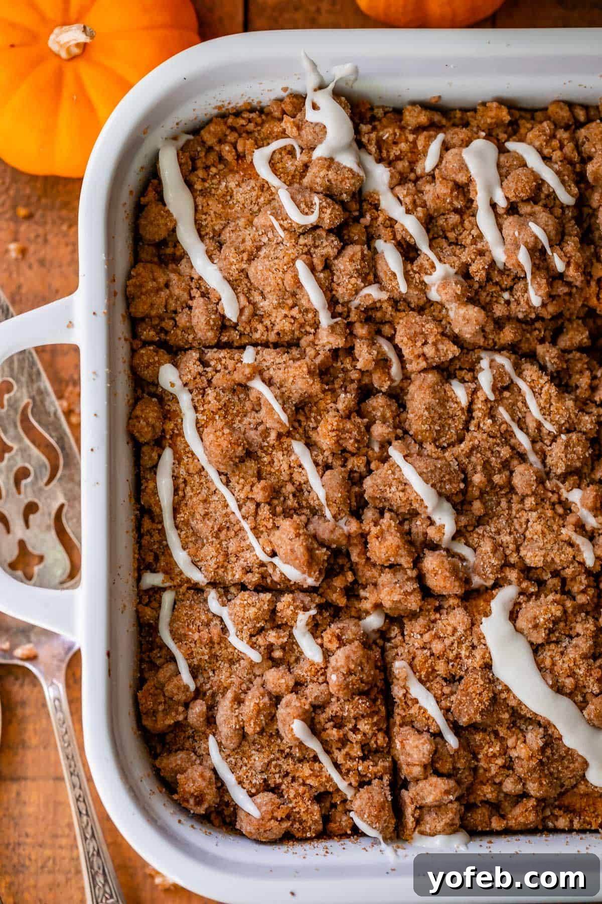 Spiced Pumpkin Crumble Coffee Cake 18 An overhead shot of a glorious pumpkin streusel coffee cake, nestled in a white baking dish, exquisitely drizzled with a sweet glaze, highlighting its inviting texture and rich autumnal color.
