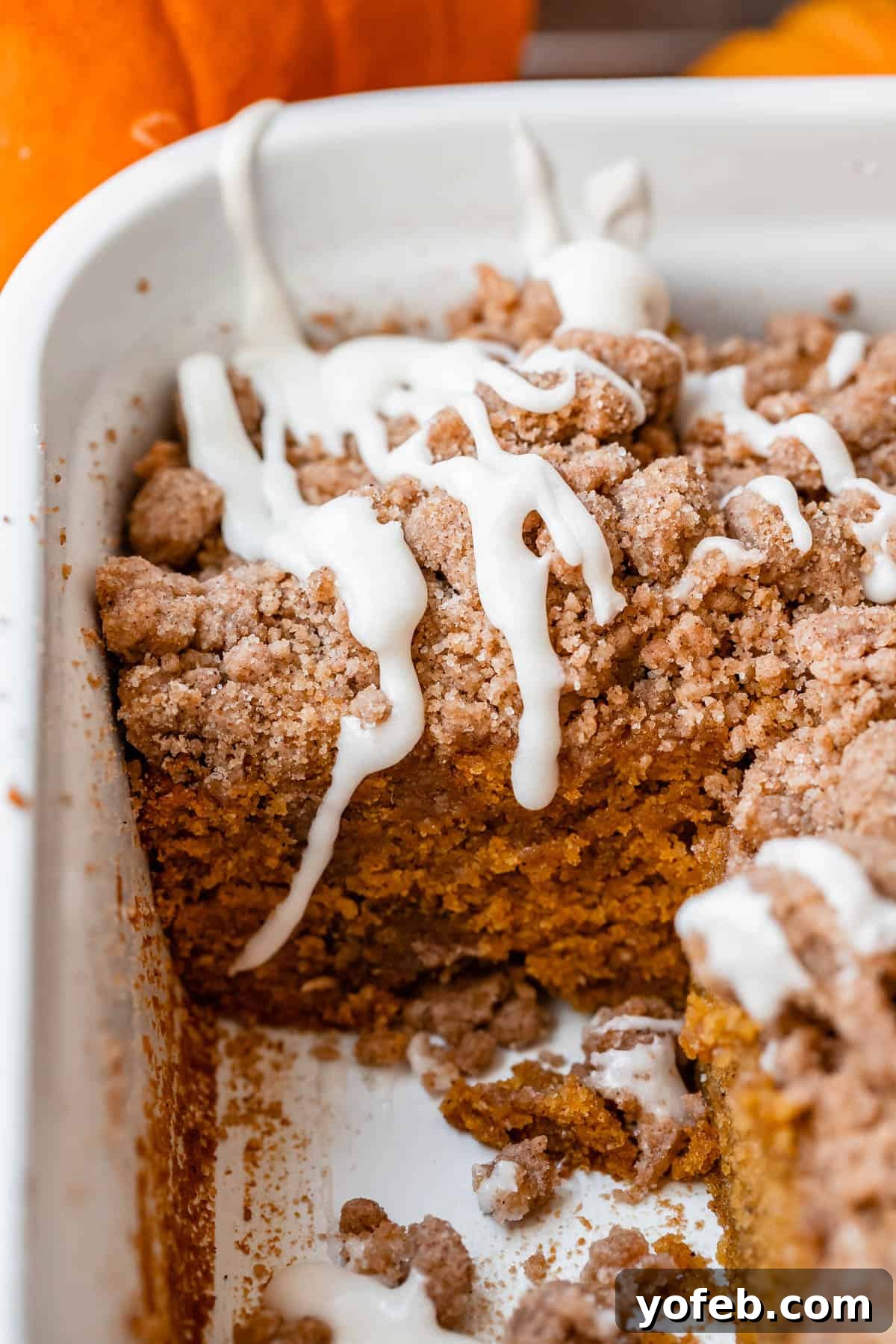Spiced Pumpkin Crumble Coffee Cake 20 A freshly baked pumpkin coffee cake in a white casserole dish, beautifully topped with a sweet glaze, ready to be enjoyed. A quintessential fall dessert.