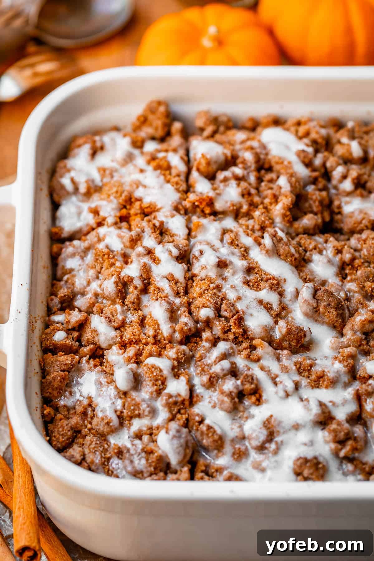 Spiced Pumpkin Crumble Coffee Cake 3 A glorious pumpkin streusel coffee cake, generously topped with a sweet glaze, sits in a white baking dish, ready to be enjoyed. A perfect treat for fall brunches and celebrations.