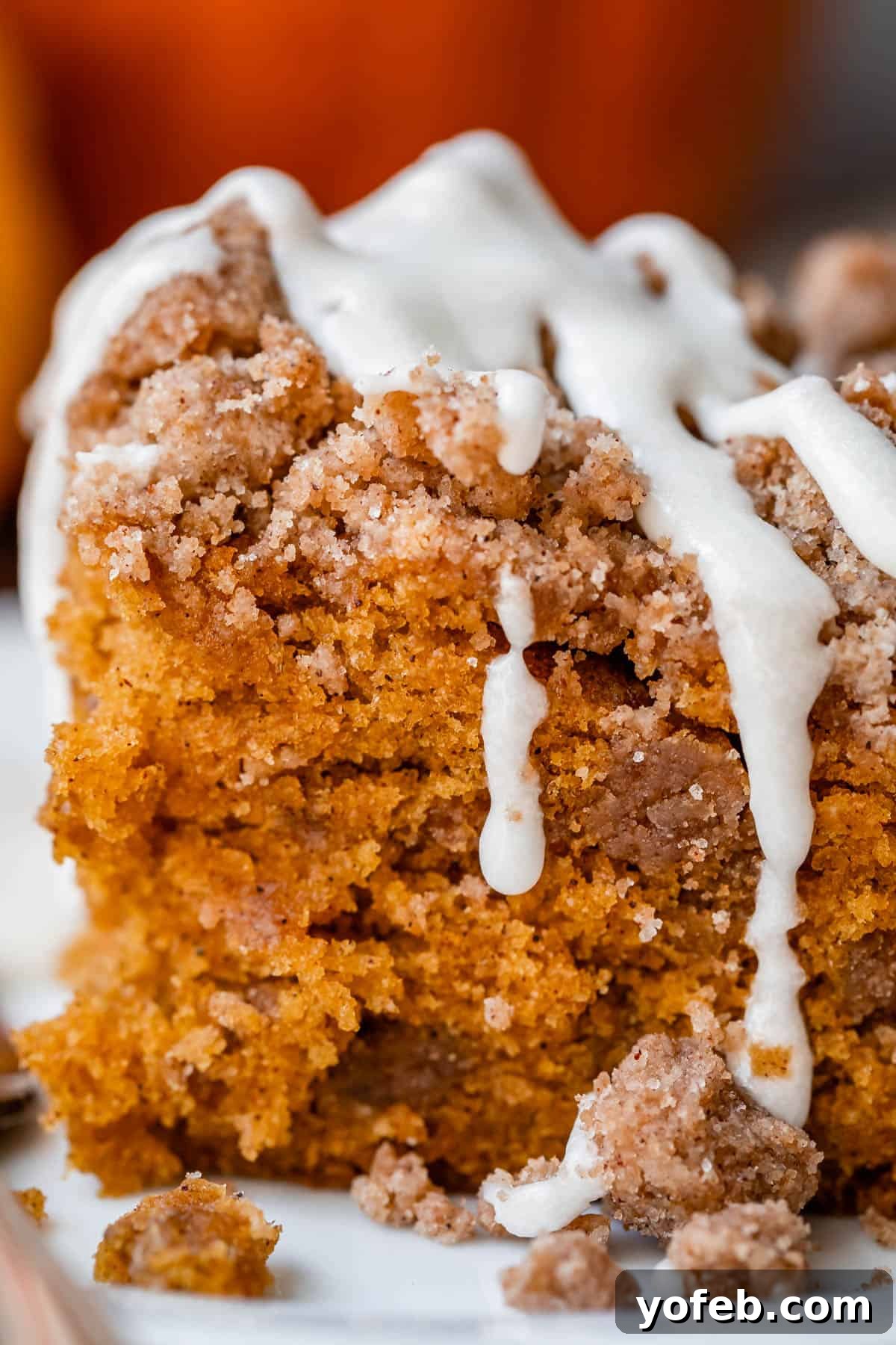 Spiced Pumpkin Crumble Coffee Cake 4 A close-up shot of a pumpkin coffee cake, glistening with a generous drizzle of glaze cascading down its sides, showcasing its moist texture and inviting warmth. Perfect for an autumn morning.