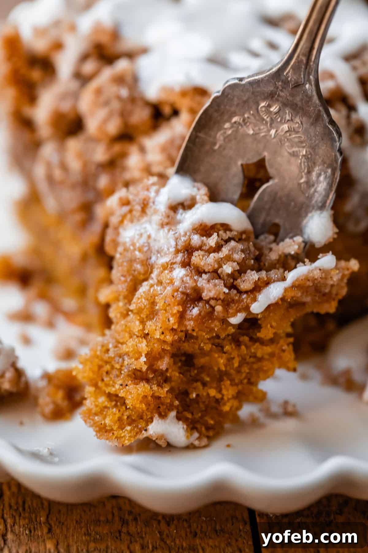 Spiced Pumpkin Crumble Coffee Cake 5 A delectable bite of pumpkin streusel coffee cake, perfectly moist with visible layers of crumble, held on a fork against a blurred background, teasing the senses with its autumn flavors.