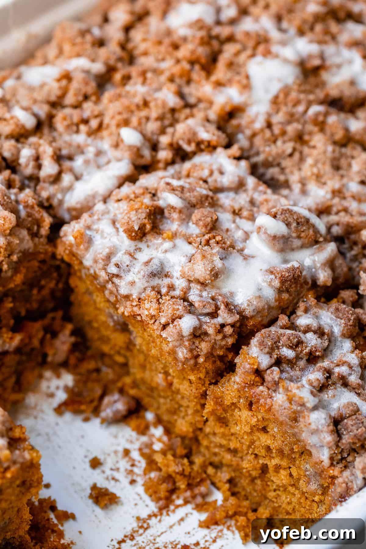 Spiced Pumpkin Crumble Coffee Cake 7 A freshly baked pumpkin coffee cake in a white baking pan, generously drizzled with glaze and ready to be served, capturing the essence of fall baking.