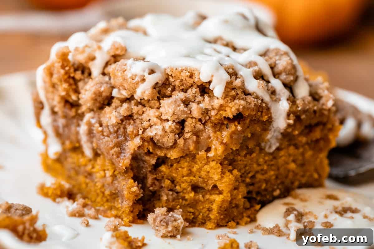 Spiced Pumpkin Crumble Coffee Cake 9 A beautiful piece of pumpkin coffee cake on a white plate with a bite taken out, revealing its moist interior and delicious streusel layers. A perfect autumn treat.