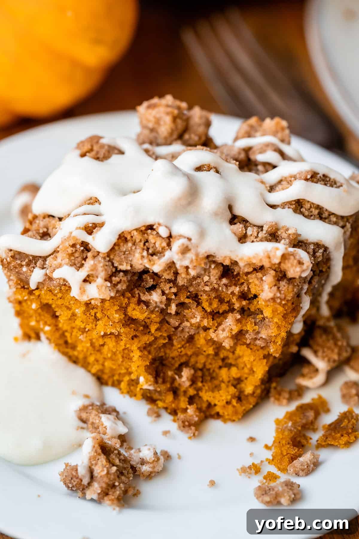 Spiced Pumpkin Crumble Coffee Cake 10 A slice of moist pumpkin coffee cake on a white plate with a fork, showing the distinct streusel layer and a hint of the sweet glaze. Perfect for a cozy autumn treat.