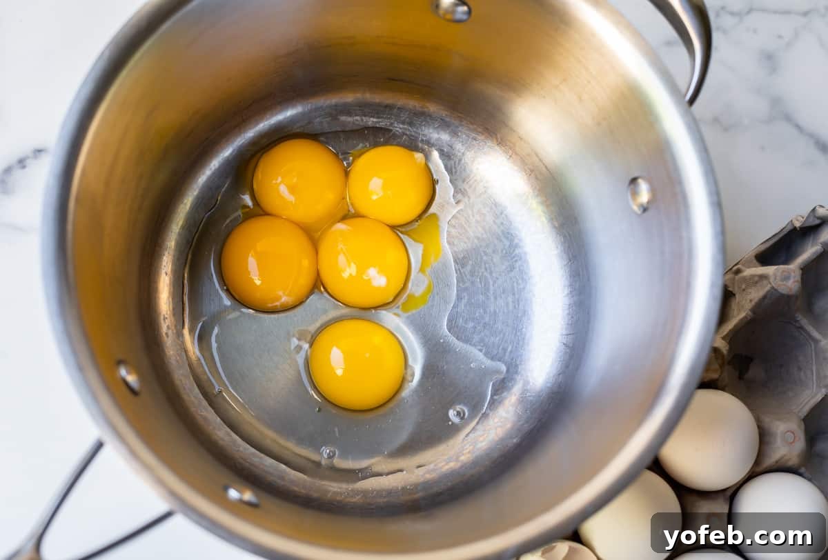 Decadent Chocolate Cream Pie Perfection 11 Five vibrant egg yolks resting in a stainless steel saucepan, ready for the next step of the pudding preparation.