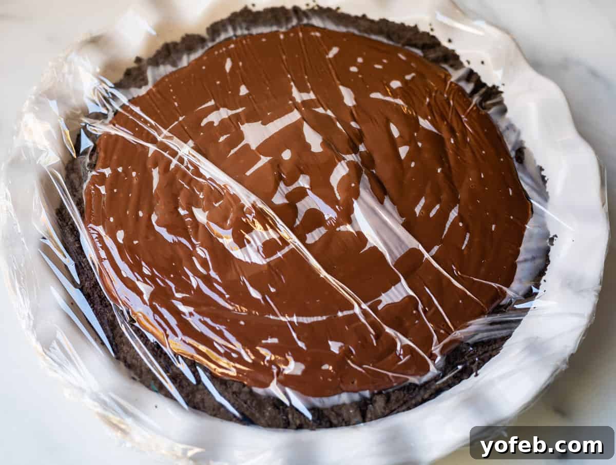 Decadent Chocolate Cream Pie Perfection 24 A freshly poured chocolate cream pie in a white dish, meticulously covered with plastic wrap pressed directly onto the pudding surface to prevent a skin from forming.
