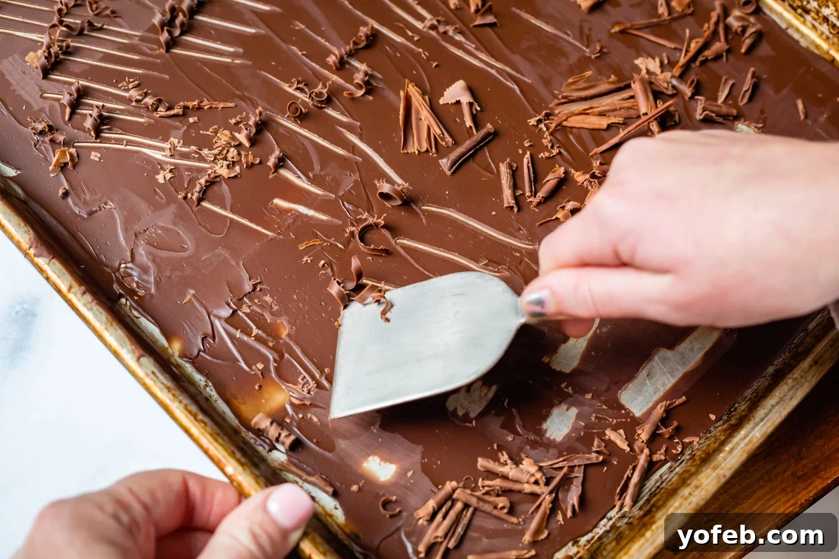 Decadent Chocolate Cream Pie Perfection 27 A metal spatula being used to delicately scrape and create perfect chocolate curls from a sheet of hardened chocolate on a baking pan.