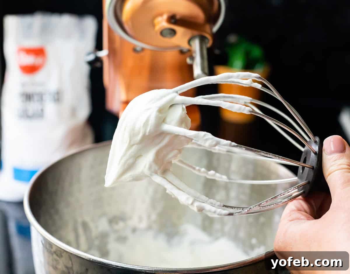 Decadent Chocolate Cream Pie Perfection 28 A whisk attachment covered in stiff, perfectly whipped cream, with a stand mixer bowl visible in the background.