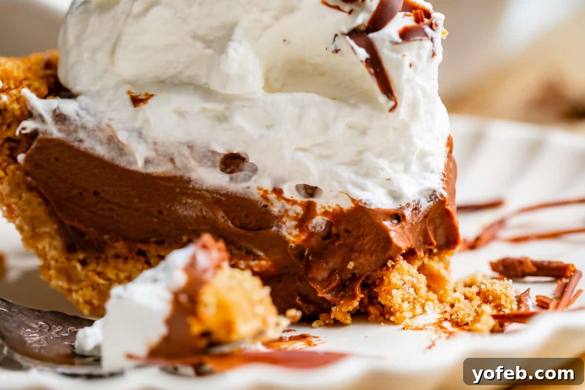 Decadent Chocolate Cream Pie Perfection 31 A slice of chocolate cream pie on a plate, with a slightly messy presentation, featuring a graham cracker crust and whipped cream.