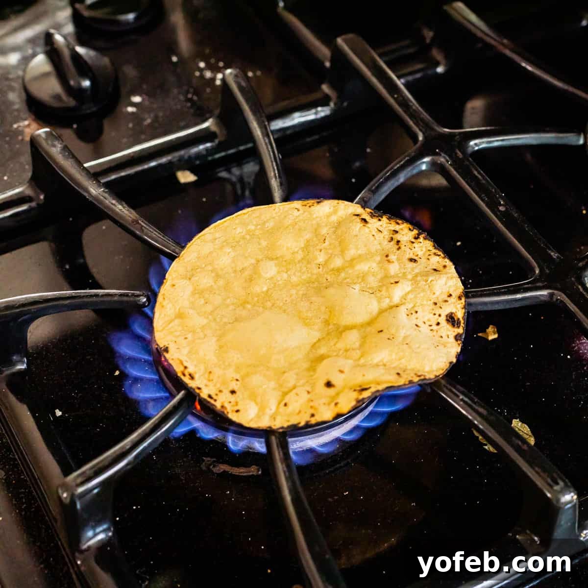 Ultimate Chicken Tacos Quick and Slow Cooker Options 16 black gas stovetop with a single corn tortilla sitting over the flame to get charred.