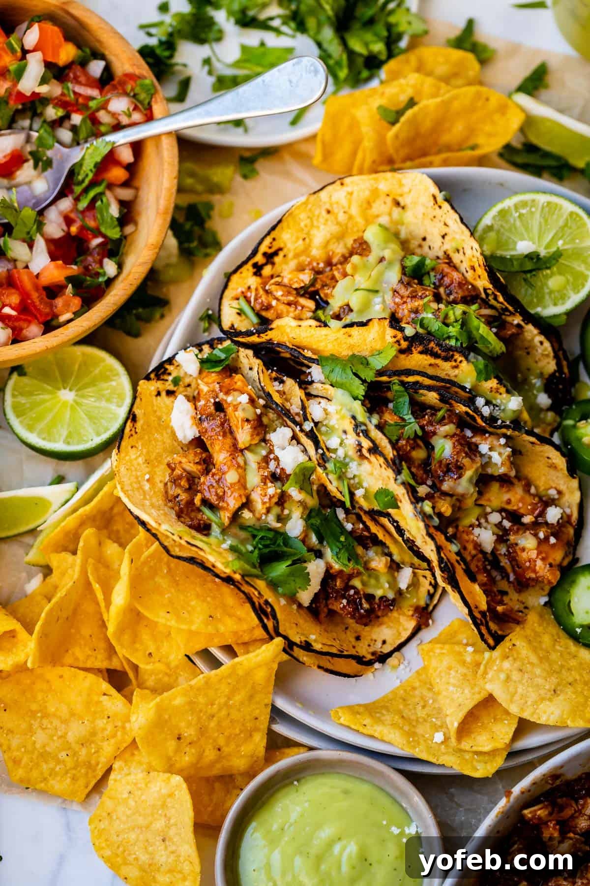 Ultimate Chicken Tacos Quick and Slow Cooker Options 4 plate with three crockpot chicken tacos with garnish on top, and chips and salsa on the side.
