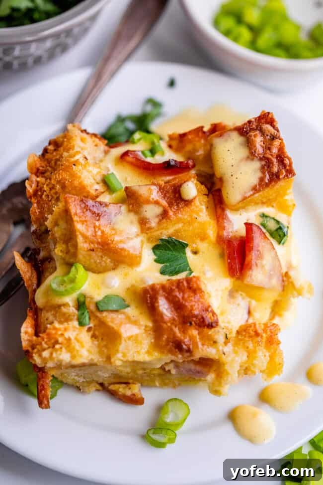 Brunch-Ready Overnight Eggs Benedict Bake 18 Overhead shot of a slice of Eggs Benedict casserole on a white plate with a fork, showing the beautiful layers and golden-brown top, inviting you to enjoy.