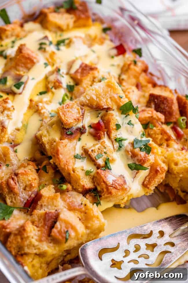 Brunch-Ready Overnight Eggs Benedict Bake 5 An Eggs Benedict bake in a clear glass casserole dish, with a silver serving spatula resting beside it, highlighting the ready-to-serve nature of this make-ahead dish.