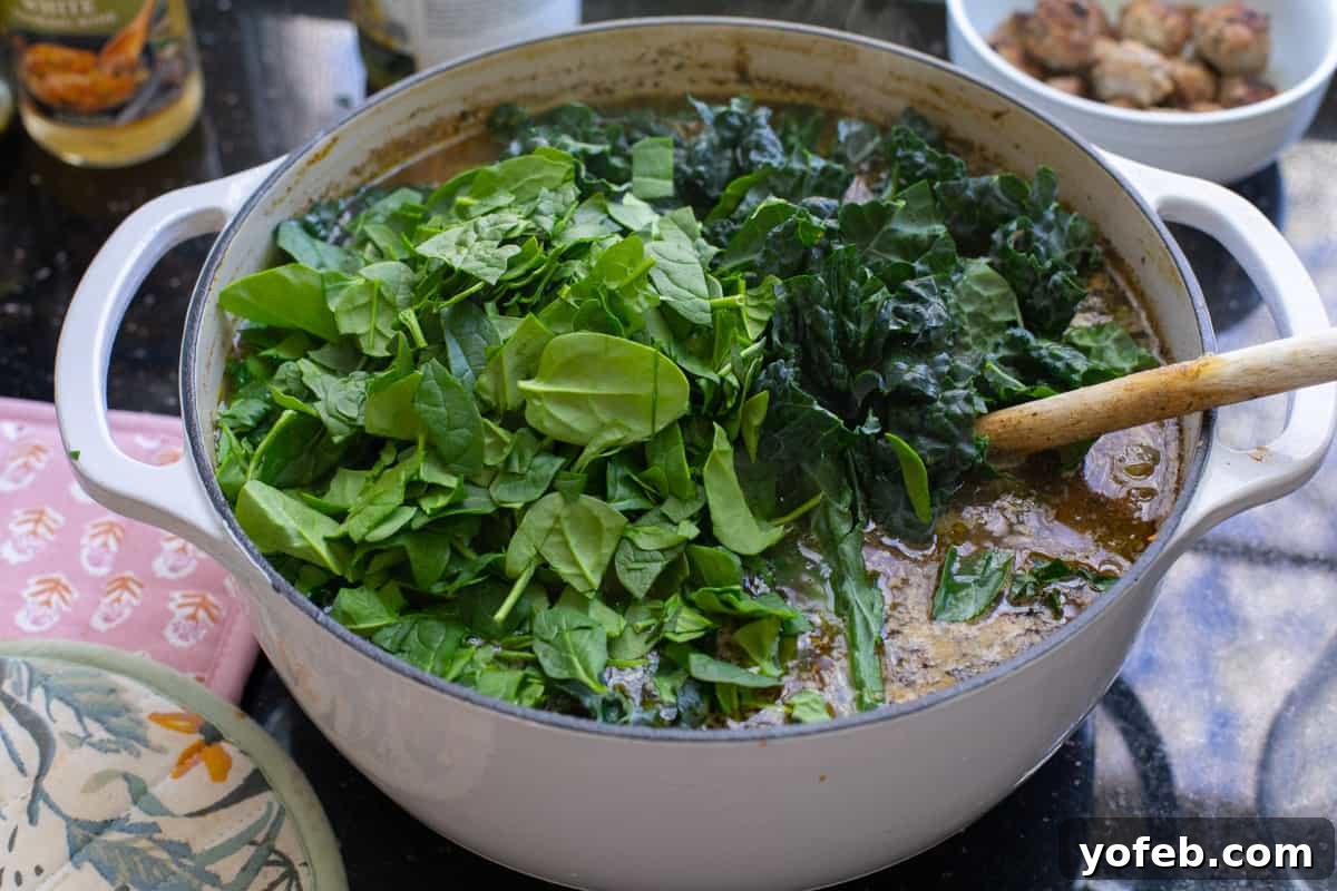 Mastering the Art of Italian Wedding Soup 22 stock pot filled with broth with a large pile of spinach and kale.