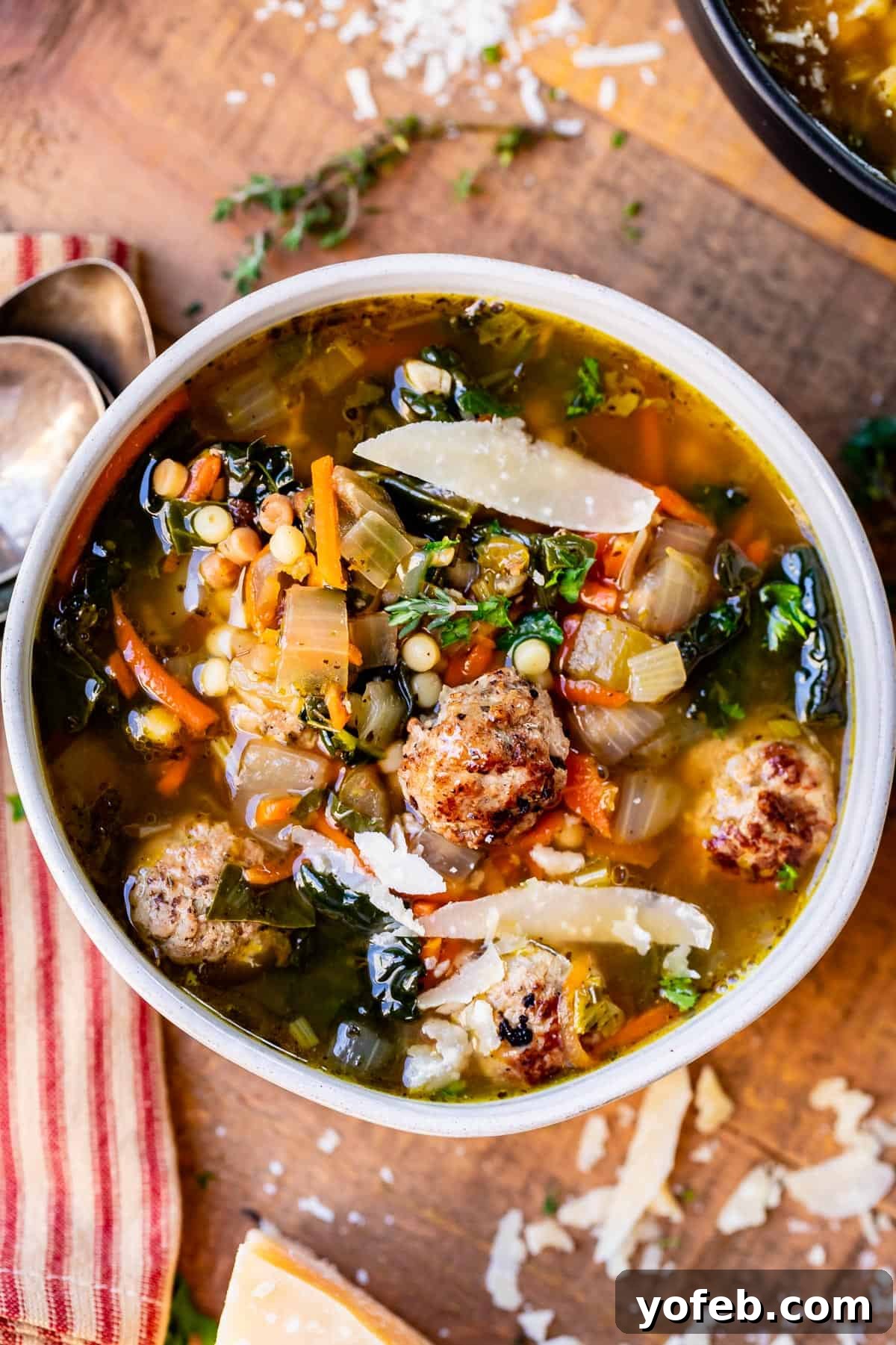Mastering the Art of Italian Wedding Soup 24 Italian Wedding Soup made of broth, meatballs, greens, and pasta in a white bowl on a cutting board.