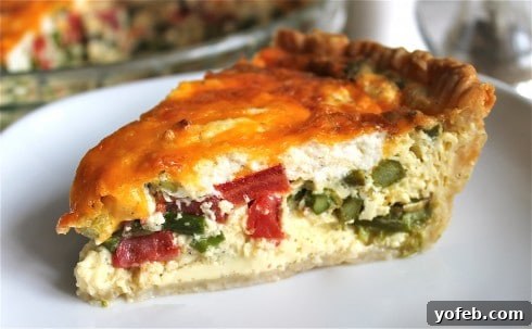 Sun-Kissed Tomato and Asparagus Quiche with Creamy Chèvre 2 Asparagus and tomato quiche slice on a white plate with full quiche in the background.