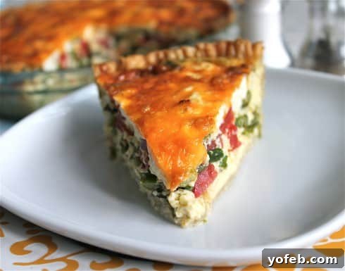 Sun-Kissed Tomato and Asparagus Quiche with Creamy Chèvre 3 Head on view of asparagus tomato and goat cheese quiche on a plain white ceramic plate over a tablecloth.
