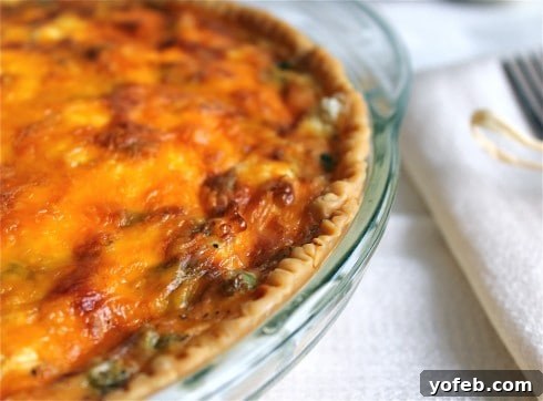 Sun-Kissed Tomato and Asparagus Quiche with Creamy Chèvre 4 Whole, baked quiche with golden brown and crispy crust in white pie dish next to white fabric napkin.