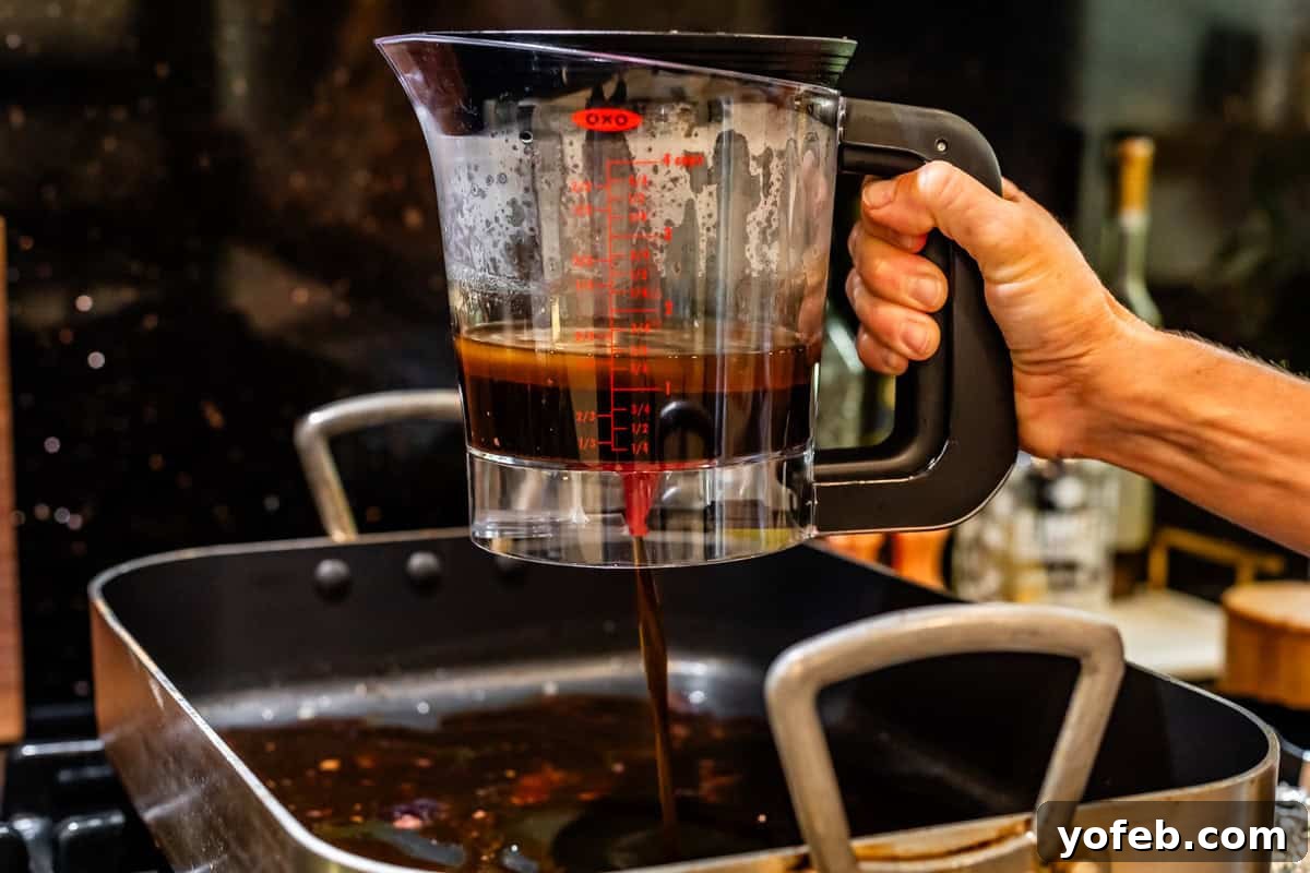 Wow Your Guests With This Perfect Prime Rib 25 A hand is shown carefully pouring only the rich broth and juices, devoid of fat, back into a clean pan, ready for gravy preparation.