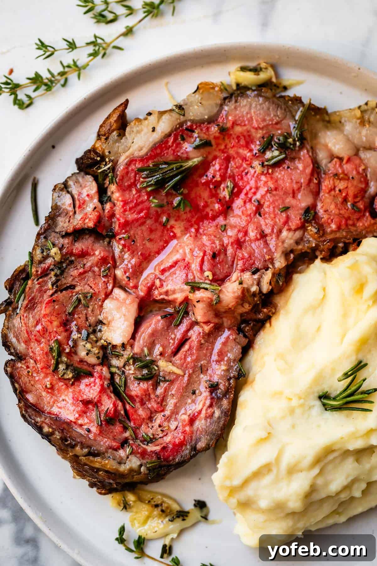 Wow Your Guests With This Perfect Prime Rib 5 A succulent slice of rare prime rib rests on a white plate, perfectly complemented by a scoop of creamy mashed potatoes beside it. This overhead shot captures the inviting warmth of a holiday meal.