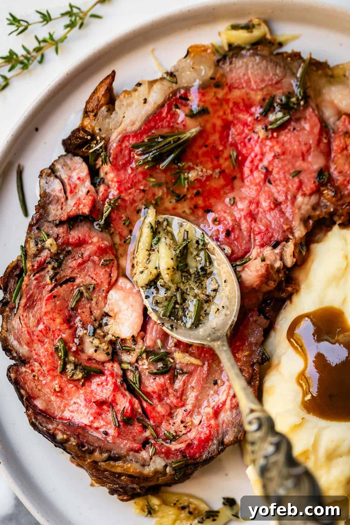 Wow Your Guests With This Perfect Prime Rib 9 A rich slice of prime rib, adorned with a luscious spoonful of garlic herb butter, presented elegantly on a white plate alongside creamy mashed potatoes and a pool of savory gravy.