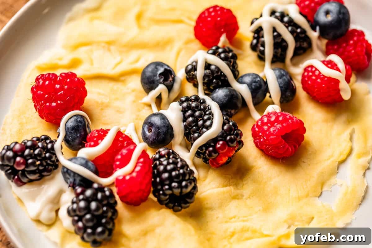 Absolutely The Best Crepes 24 A delicate crepe beautifully presented on a plate, generously topped with a medley of fresh mixed berries and drizzled with a creamy, sweet spread. An irresistible treat for any time of day.