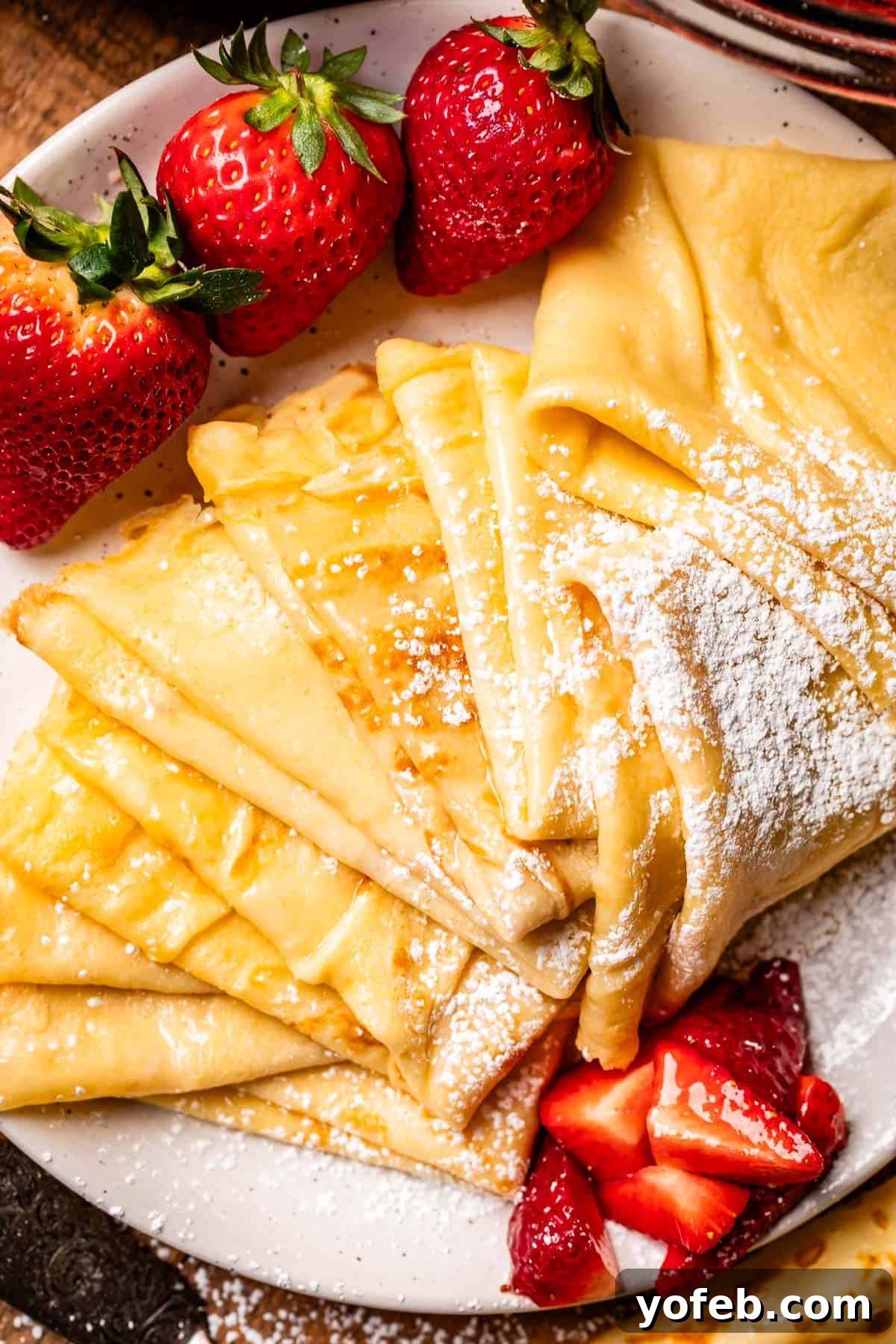 Absolutely The Best Crepes 9 A pristine ceramic plate artfully arranged with quarter-folded crepes and a vibrant side of fresh, whole strawberries. The perfect presentation for a classic and delightful treat.