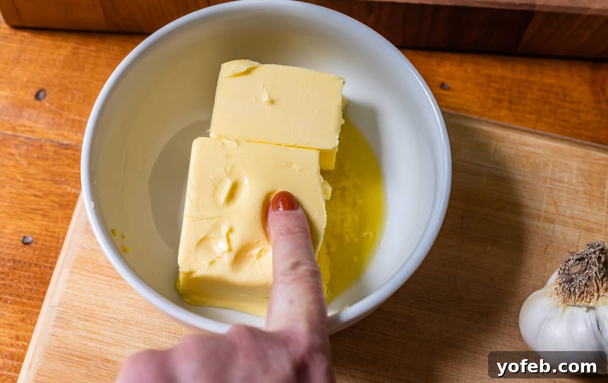 Irresistible Garlic Butter Loaf 9 Close-up of a finger pressing into softened butter in a bowl, demonstrating the ideal consistency for garlic bread.