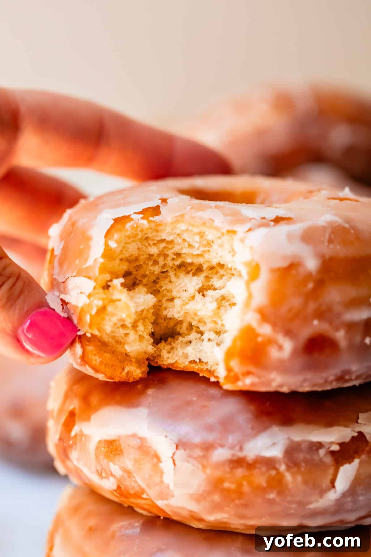 Doughnut Delights from Scratch 2 Close-up of a hand reaching for a freshly made, fluffy glazed donut with a bite taken out of it, showcasing its perfect texture.