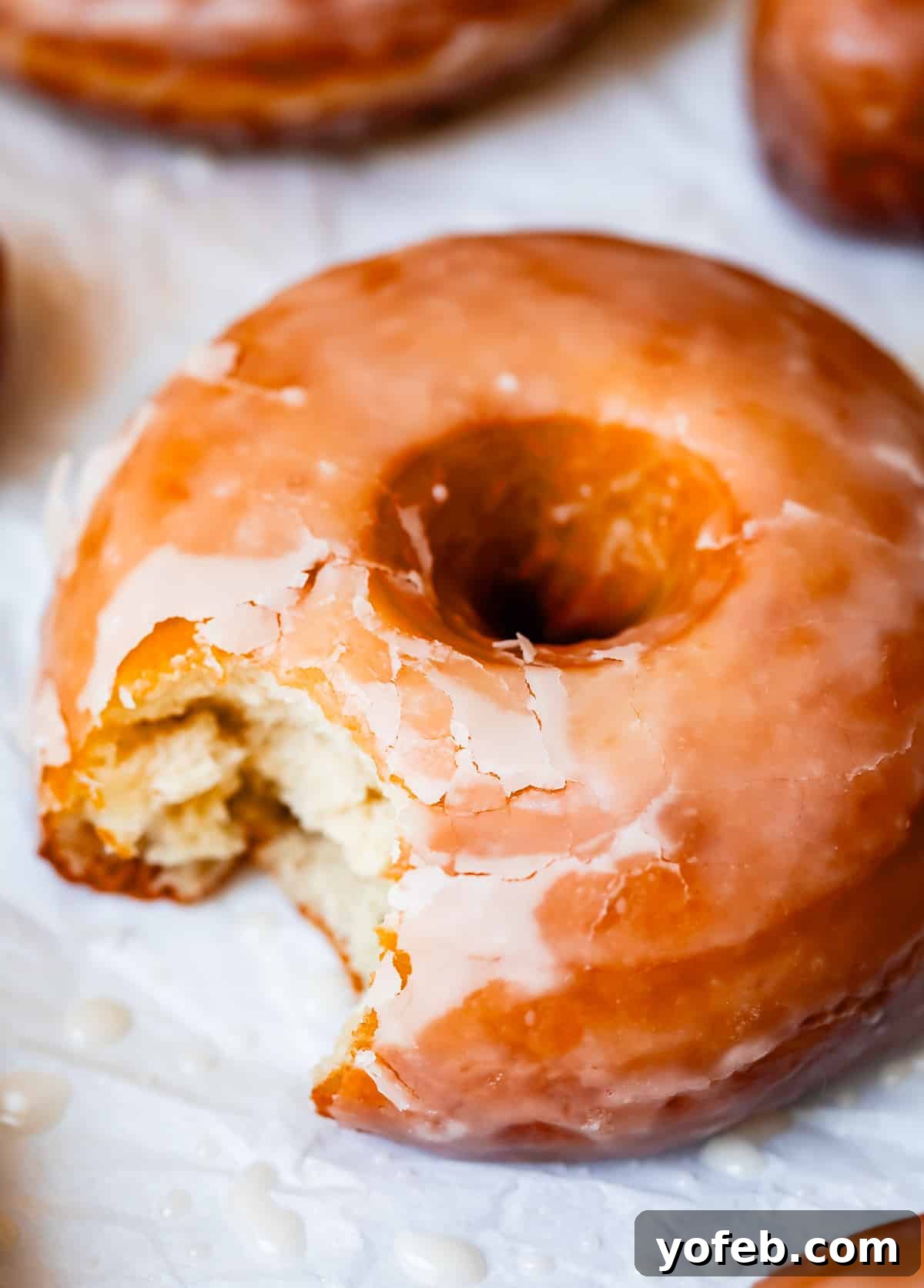 Doughnut Delights from Scratch 4 A homemade glazed donut with a bite taken out of it, resting on a piece of parchment paper, highlighting its soft interior.